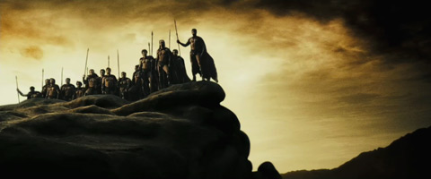 The Spartans stand atop a cliff, nearly silhouetted against the gold sky.