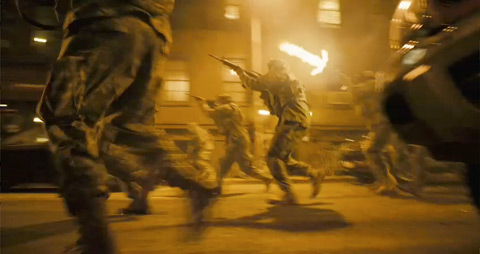 Soldiers, seen from the side, run up a street firing their rifles.