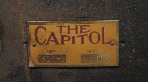 An old metal plate fastened to worn black metal. The plate reads The Capitol, and displays the serial number and size code.
