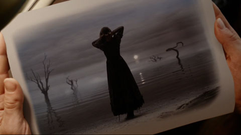 In a picture held by two hands, Violet ties her hair back by the sea.