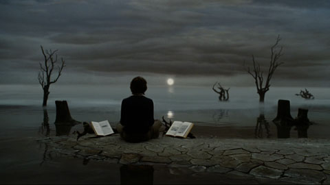 Klaus sits at the edge of a misty sea, looking out on dead trees and a waning sun amongst grey clouds.