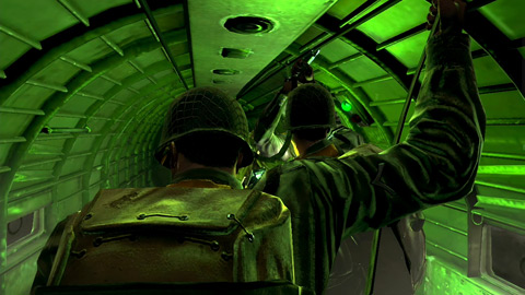 Your view behind your fellow paratroopers, who are standing up in line ready to jump. The plane cabin is flooded with green light from the jump light.