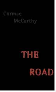 The cover of 'The Road', which is written in red distressed letters along with Cormac McCarthy's name in dark grey letters, all of which sits on a black backdrop.