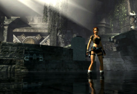 Lara stands in shallow water in a ruin as light streams in from above. Some large stone mechanical elements are visible behind some hanging foliage.