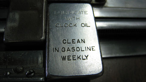 An inscription in all caps san serif letters on brushed metal that reads: Lubricate in clock oil. Clean in gasoline weekly.