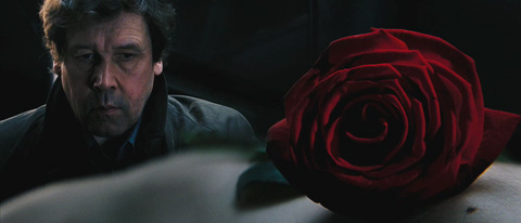 Finch looks at a body, on top of which is a blood-red rose that sits in the foreground.