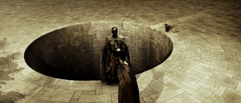 Leonidas points his sword at the Perisan emmisary, who is at the lip of a large open well.
