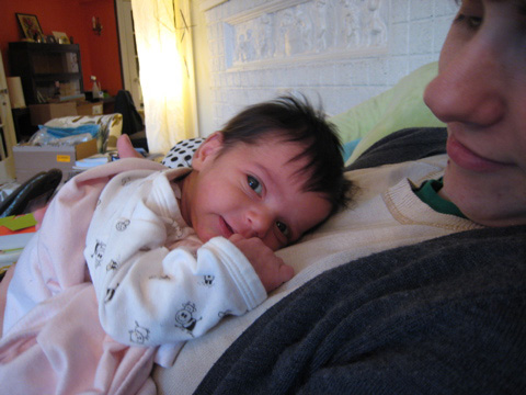 Blackbird lays on Mom's chest, wrapped in a blanket and looking satisfied.