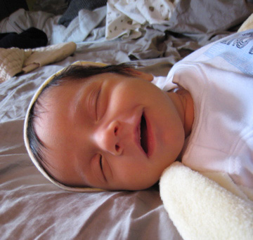 Blackbird laying on her side in our bed, wearing a hat and smiling in her sleep.