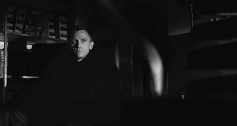 Shown in black and white, James Bond's pale face stands out from the darkness of a low-lit office.