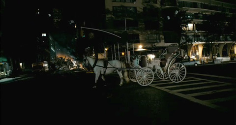 A riderless carriage, drawn by a white horse, moves down an empty street, with flaming debris in the distance.