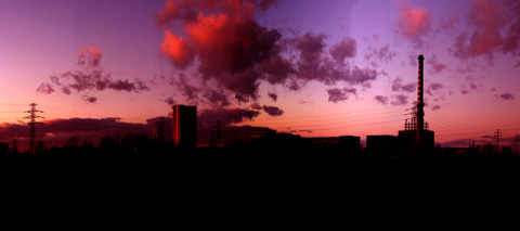 A coal mine, seen silhouetted on the horizon at sunset, with clouds in the sky.