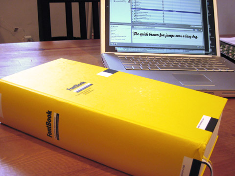 FontBook, laying in front of an Apple titanium PowerBook on a wooden table.
