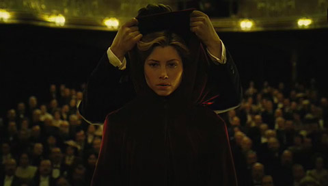 Sophie is hooded in a red cloak on stage, looking away from the audience.