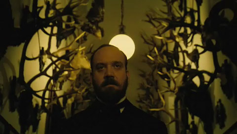 The Chief Inspector, looking stern, walks down a hall festooned with antlers and sparingly lit.