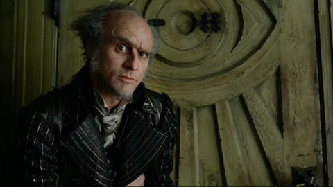 Count Olaf in front of his front door, which is carved with an eye motif.