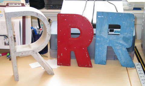 Three metal sign capital Rs. One brushed aluminum, one blue and blocky, one red and geometric grotesque, I think.
