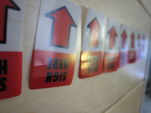 A line of sign here arrow tags on a wooden surface.