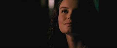 Louis Lane's face, lit on one side, as she looks up smiling at night.