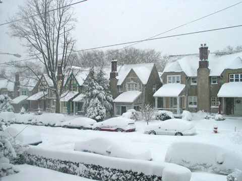 Deep snow on a row of houses, the street, and car in our neighborhood and still falling
