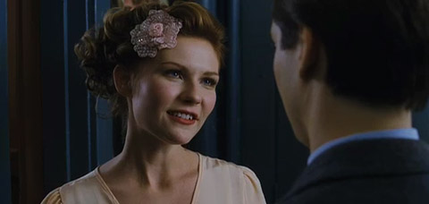 Mary Jane Watson, wearing a dress and flower-shaped ornament in her hair, talks to Peter.