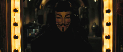 V puts on his mask in front of a dressing room mirror.